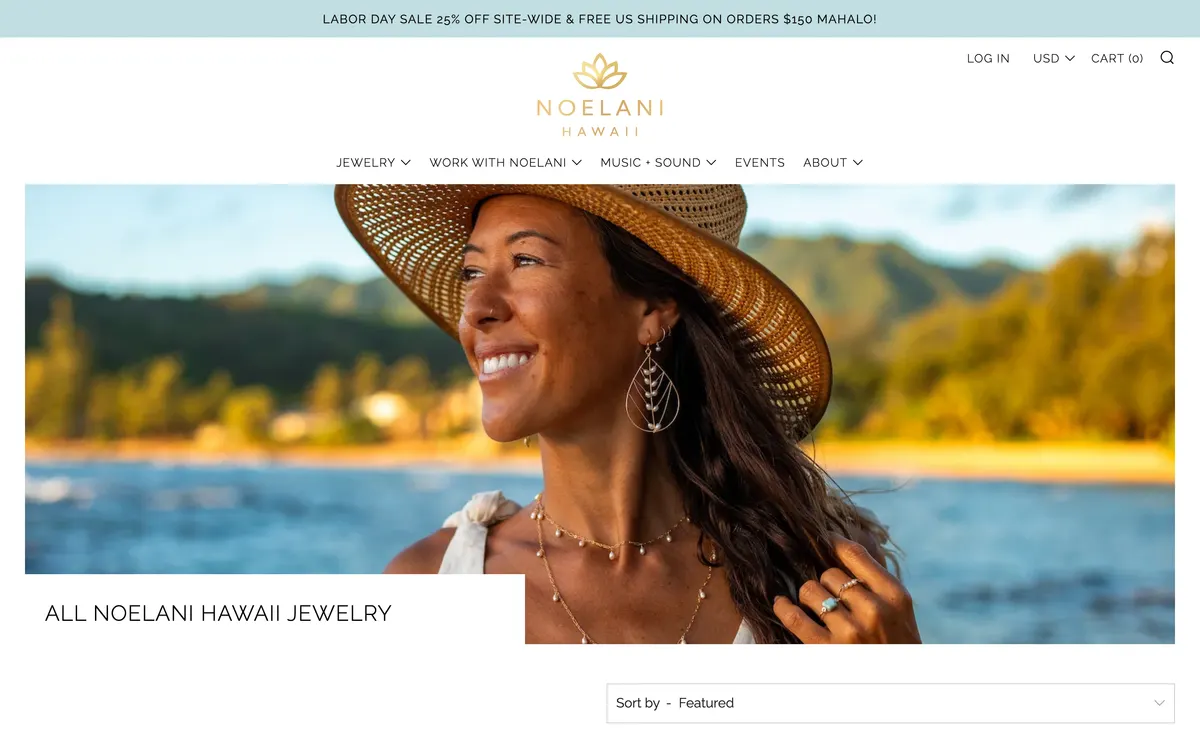 The All Noelani Hawaii Jewelry collection page on desktop with the popup dismissed, showing a large soft-focus landscape banner filling the screen, the collection title beneath it, and a Sort by dropdown at the bottom edge.